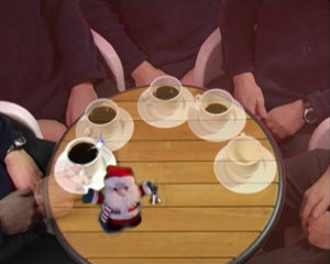 Videostill of a man sitting at a table with coffee and a santa claus doll.